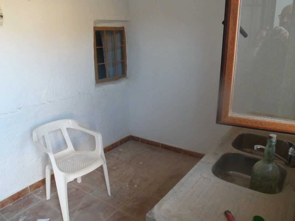 Charming cave house interior in Freila, Granada, featuring rustic walls, small window, and simple fu.