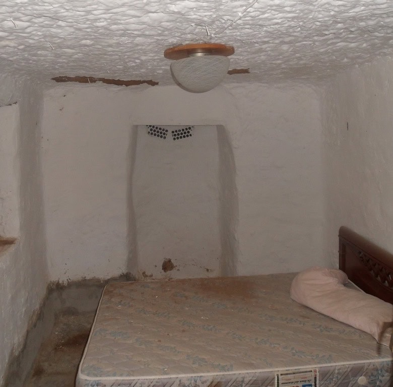 Cozy cave house bedroom with whitewashed walls and rustic wooden bed in Freila, Granada.