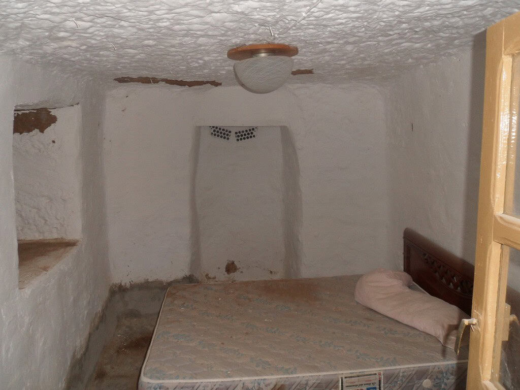 Cozy cave house bedroom with whitewashed walls and rustic wooden bed in Freila, Granada.