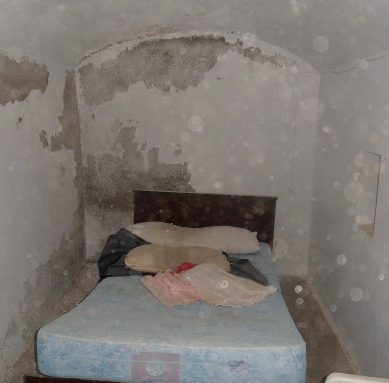 Cave house bedroom with worn walls and simple bedding in Freila, Granada.