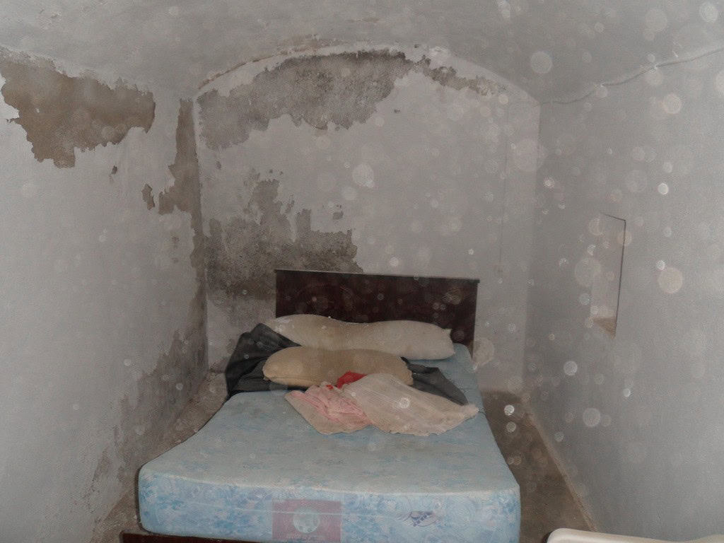 Cave house bedroom with worn walls and simple bedding in Freila, Granada.