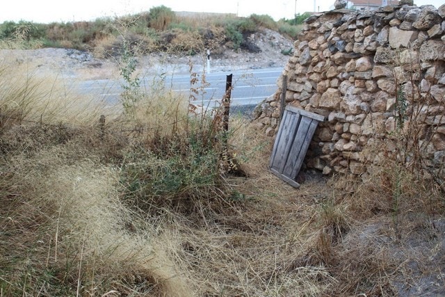 Rural property site in Hijate, Almeria with stone wall and overgrown vegetation.