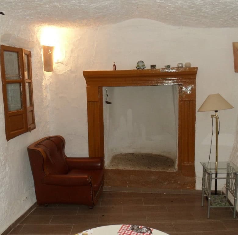 Cave house interior with rustic fireplace, leather armchair, and cozy decor in Freila, Granada.