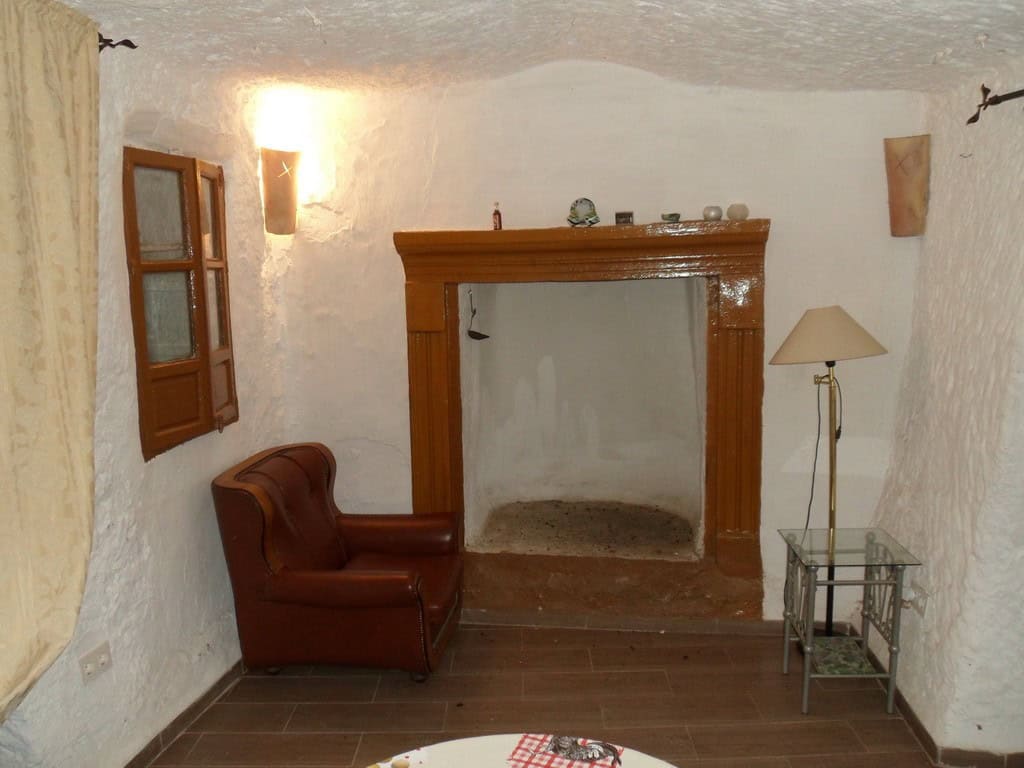 Cave house interior with rustic fireplace, leather armchair, and cozy decor in Freila, Granada.