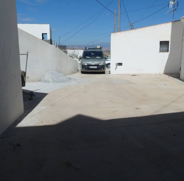 Cave house in Freila, Granada, with a parking area and whitewashed walls under a clear blue sky.