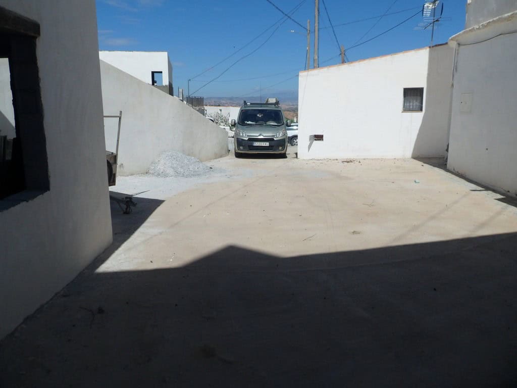 Cave house in Freila, Granada, with a parking area and whitewashed walls under a clear blue sky.