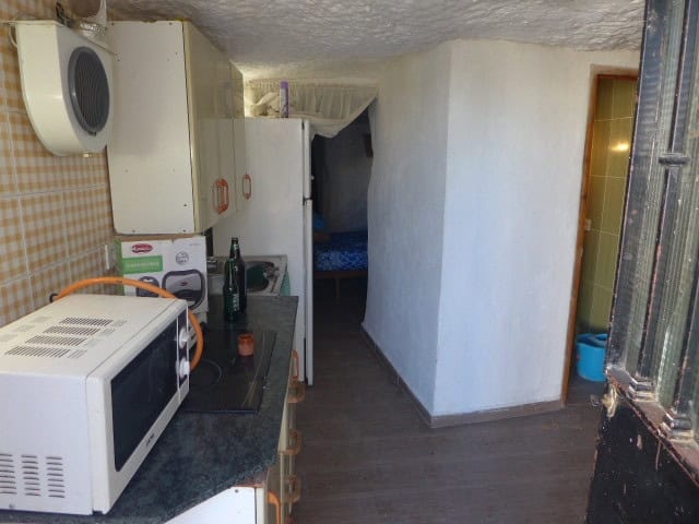Cave house interior with compact kitchen and sleeping area in Freila, Granada, offering rustic charm.