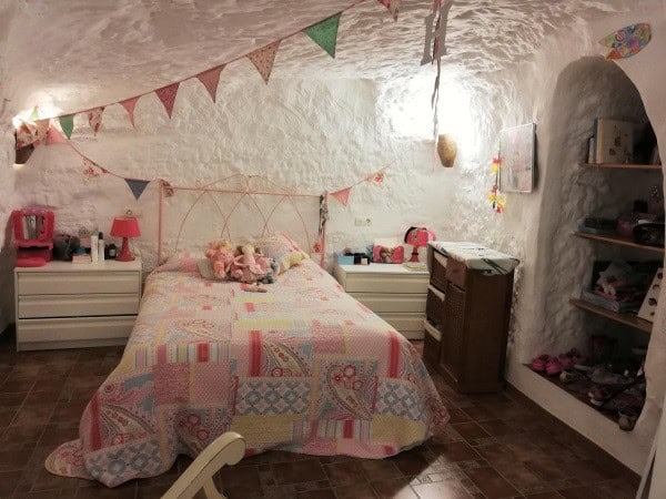 Charming cave house bedroom with colorful quilt, bunting decorations, and rustic furniture in Galera.