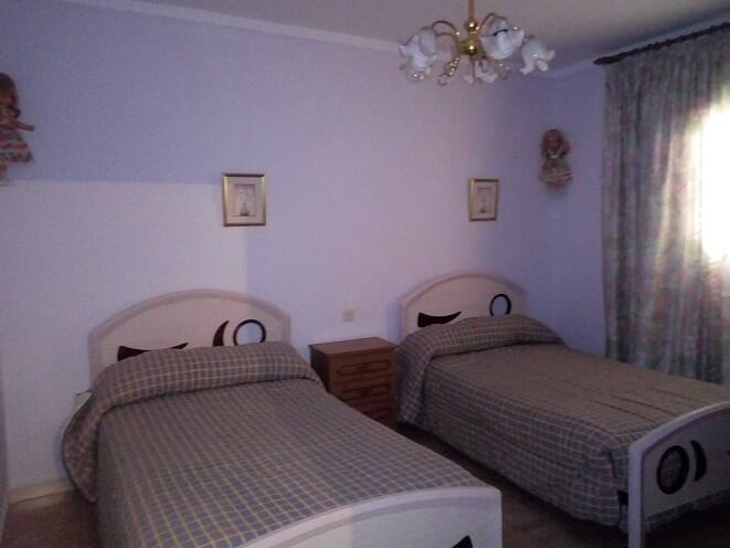 Twin bedroom with two beds, wooden nightstand, and floral curtains in Tijola village home.