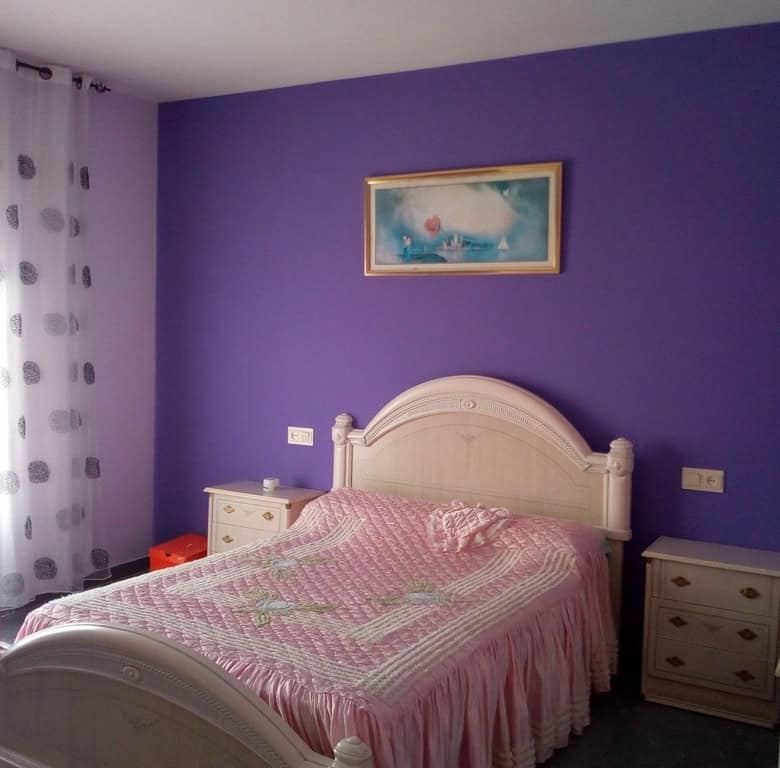 Charming bedroom with purple walls and a white bed in Cela, Almeria, ideal for a peaceful village li.