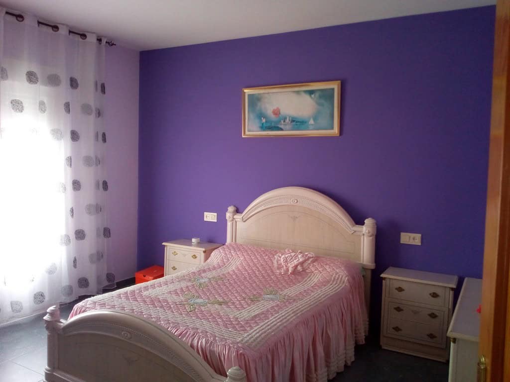 Charming bedroom with purple walls and a white bed in Cela, Almeria, ideal for a peaceful village li.