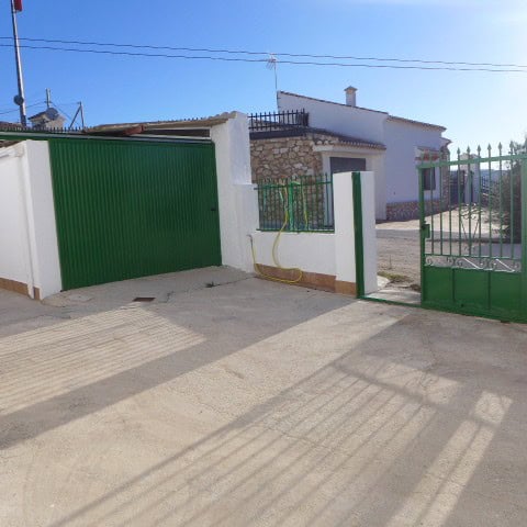 Cave house in Galera, Granada with white walls and green gates, set in a rural area with clear blue.