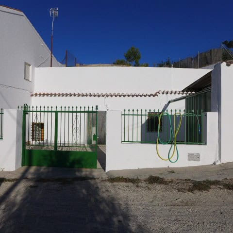 Cave house in Galera, Granada with white walls and green gate, set against a clear blue sky.