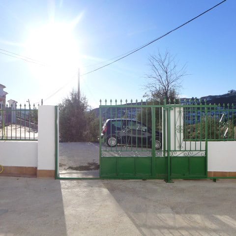Cave house with a green gate in Galera, Granada, under bright sunlight, surrounded by trees and a pa.