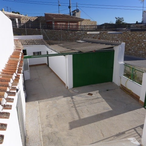 Cave house in Galera, Granada with white walls and green gate, set in a rural area with stone houses.