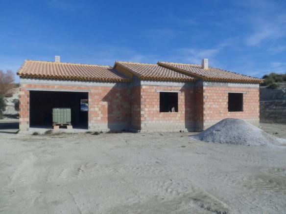 Farm property in Benamaurel, Granada, with unfinished brick walls and tiled roof, set against a clea.
