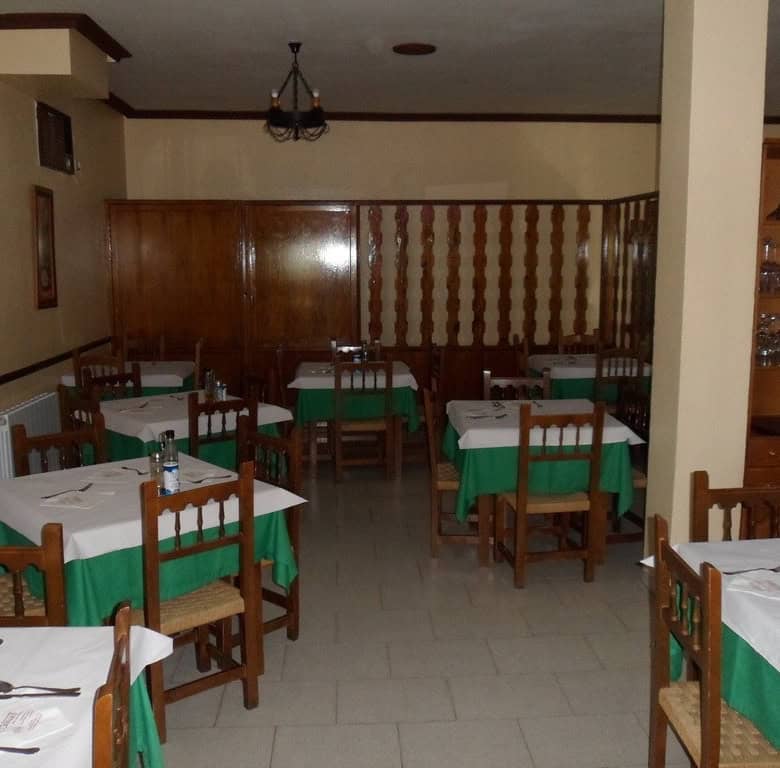 Interior of a traditional restaurant in Baza, Granada, featuring wooden furniture and green tableclo.
