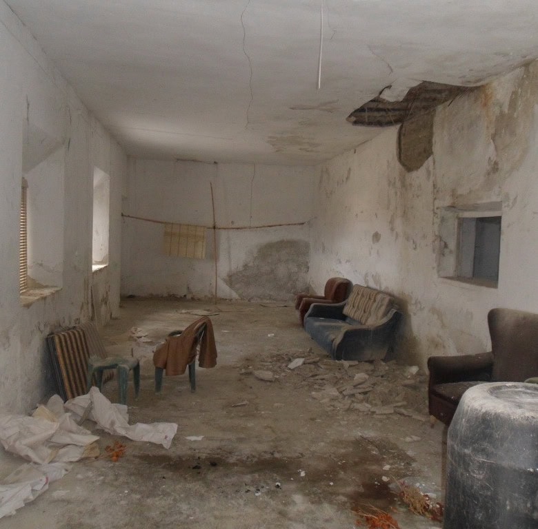 Cave house interior with worn furniture and damaged walls in Baza, Granada.
