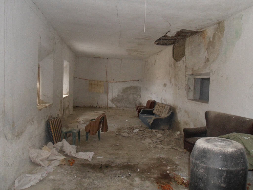 Cave house interior with worn furniture and damaged walls in Baza, Granada.