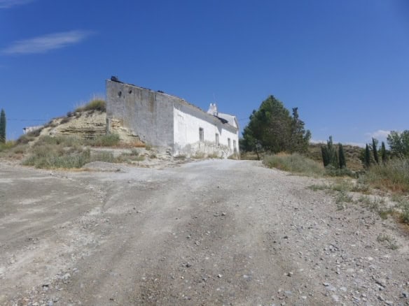 Traditional cave house in Baza, Granada, set in a rural landscape with clear blue skies.