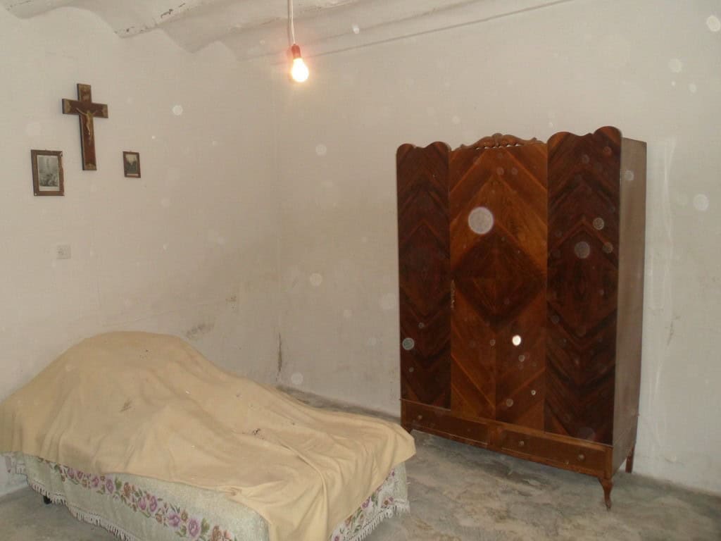 Charming bedroom in a rural property in Baza, Granada, featuring a simple bed, wooden wardrobe, and.