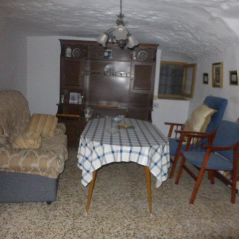 Cave house living room with vintage furniture, wooden cabinet, and a dining table in Galera, Granada.