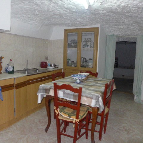 Cave house kitchen with wooden cabinets, dining table, and chairs in Galera, Granada.