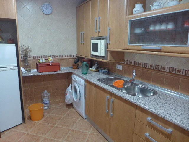 Kitchen with wooden cabinets, sink, microwave, and washing machine in Freila, Granada.