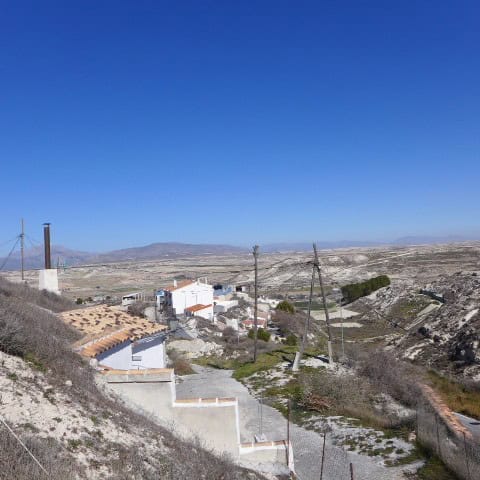 Cave house in Orce, Granada, set in a rugged landscape with clear blue skies.