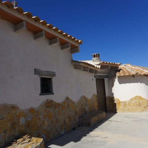 Traditional cave house in Orce, Granada with white walls and stone accents under a clear blue sky.