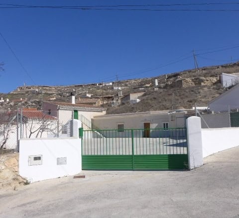Cave house in Orce, Granada with white walls and green gate, set against a hillside with clear blue.