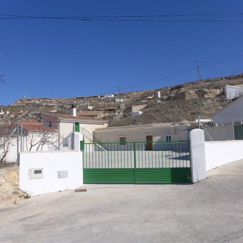 Cave house in Orce, Granada with white walls and green gate, set against a hillside with clear blue.