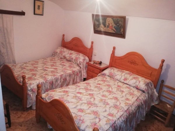 Cave house bedroom with two wooden beds and floral bedspreads in Orce, Granada.