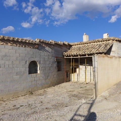Cave house in Huescar, Granada with traditional stone walls and tiled roof, set against a bright blu.