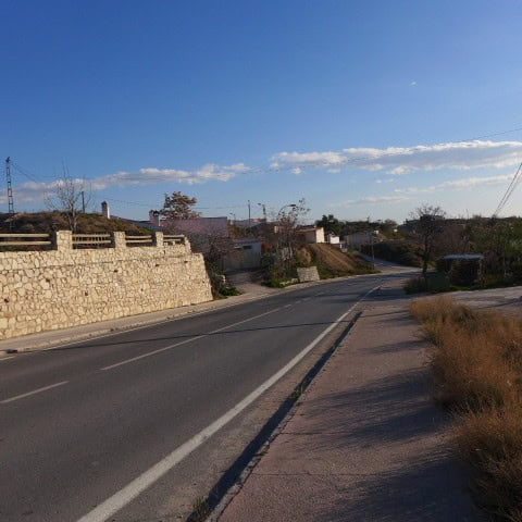 Scenic view of a rural road near a cave house in Huescar, Granada, under a clear blue sky.