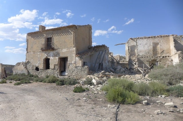Abandoned stone house with damaged walls and surrounding ruins in a rural setting.