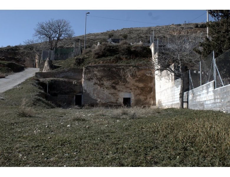 Cave house in Baza, Granada, set on a hillside with surrounding fencing and natural landscape.