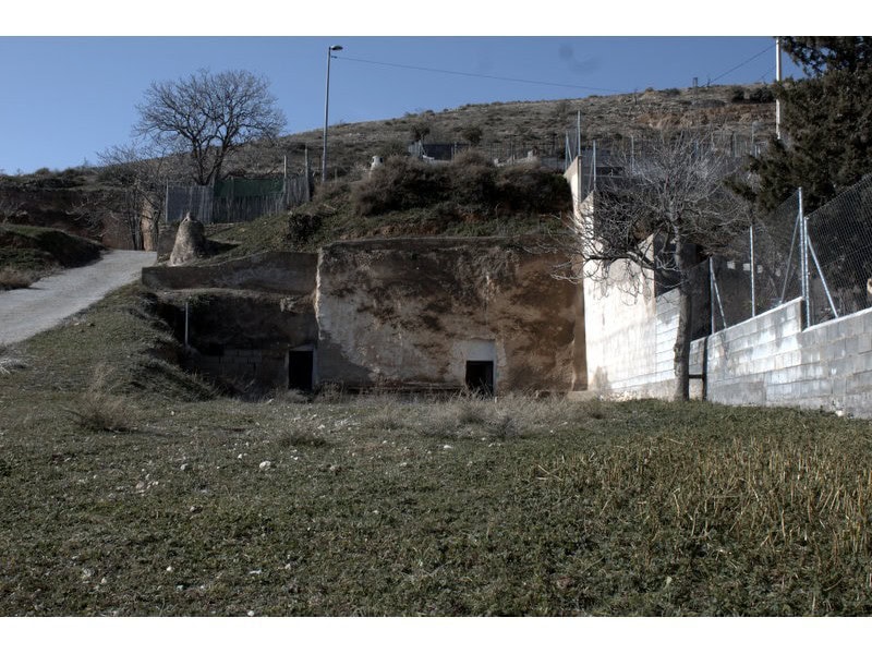 Cave house in Baza, Granada, set on a hillside with surrounding fencing and natural landscape.