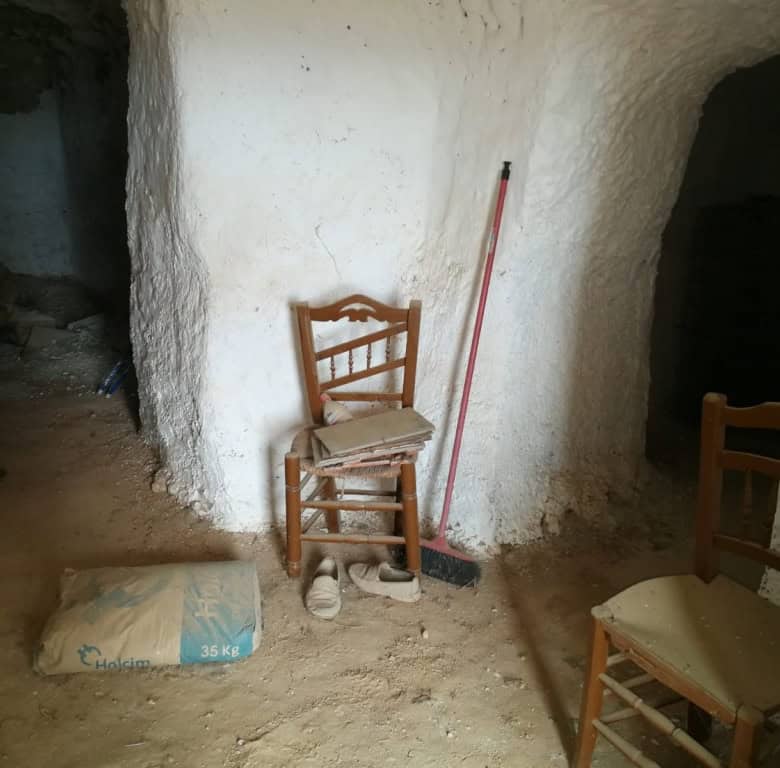 Charming cave house interior in Baza, Granada, with rustic wooden chairs and natural stone walls.