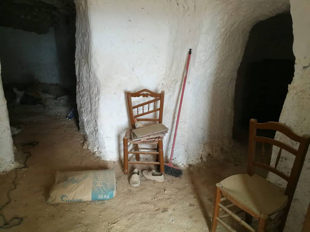 Charming cave house interior in Baza, Granada, with rustic wooden chairs and natural stone walls.