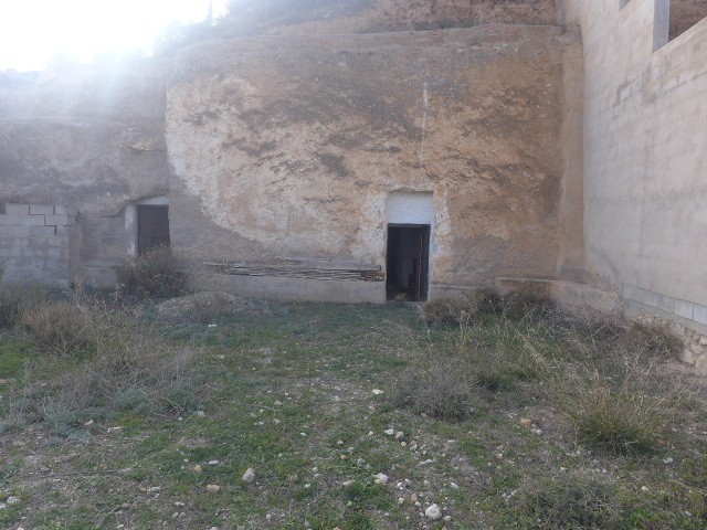 Cave house entrance in Baza, Granada, with natural rock walls and surrounding terrain.