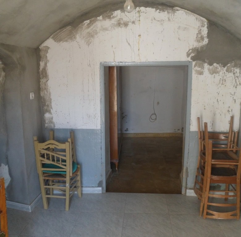 Cave house interior in Guadix, Granada, showcasing rustic stone walls and wooden chairs.