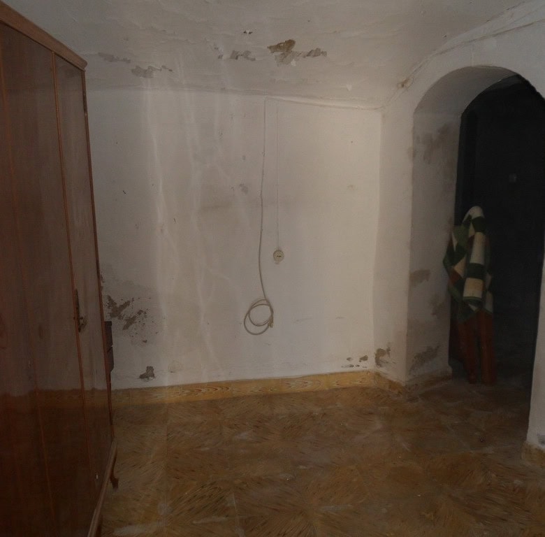 Interior of a rustic cave house in Guadix, Granada with simple walls and arched doorway.
