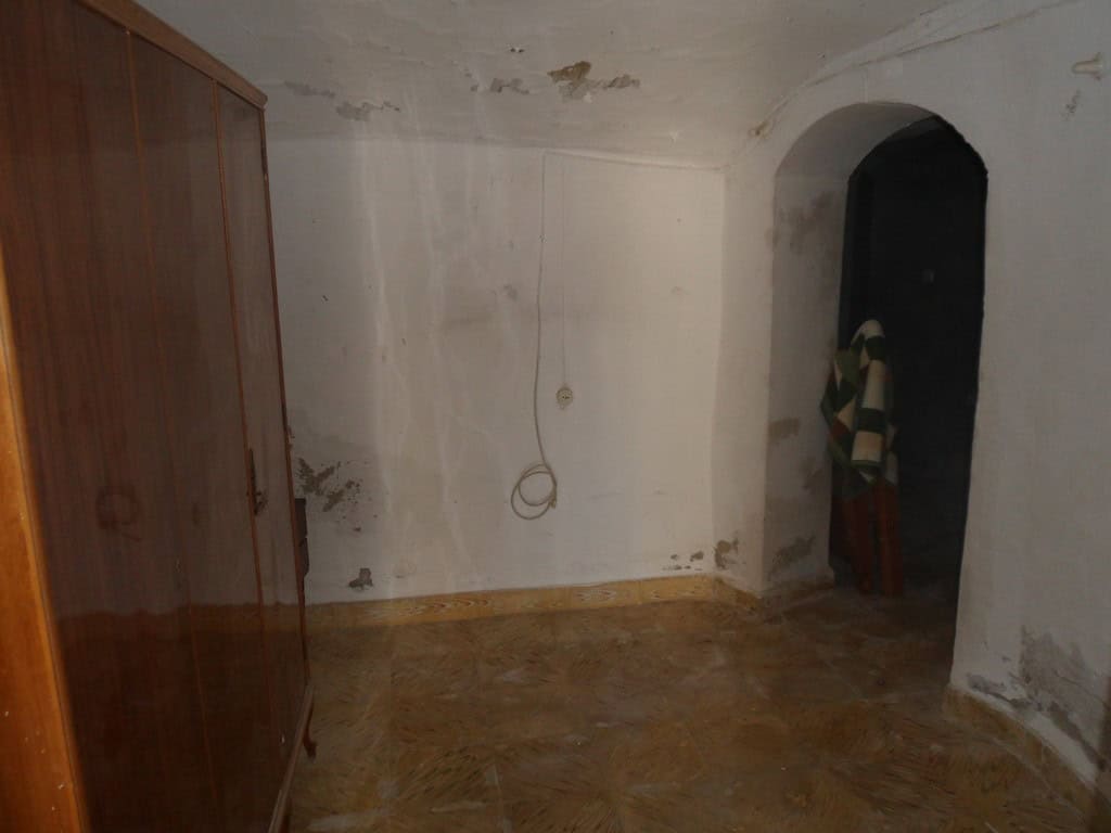 Interior of a rustic cave house in Guadix, Granada with simple walls and arched doorway.