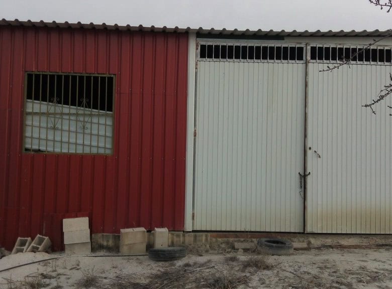 Commercial building in Cortes de Baza, Granada with metal doors and red exterior.
