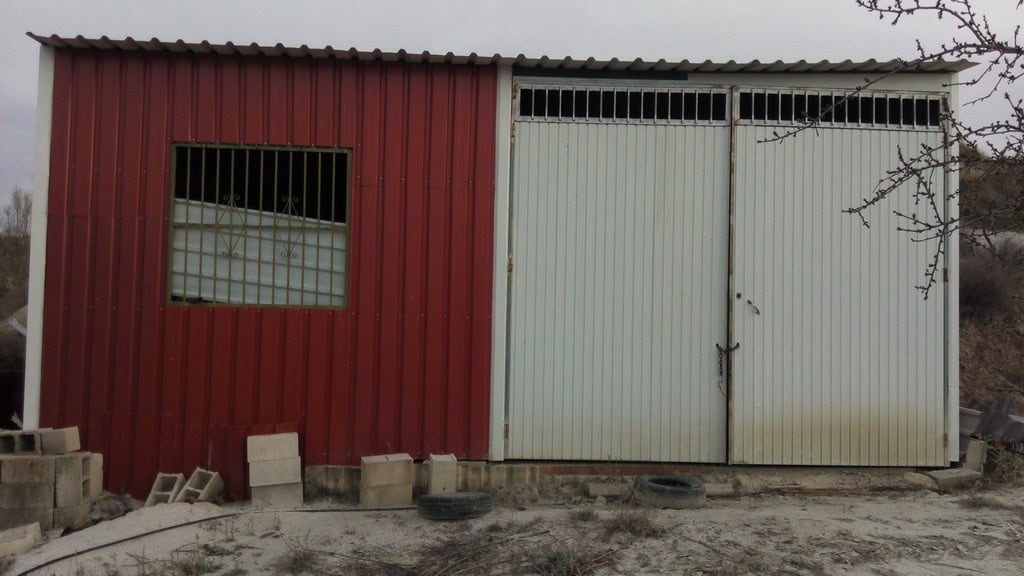 Commercial building in Cortes de Baza, Granada with metal doors and red exterior.