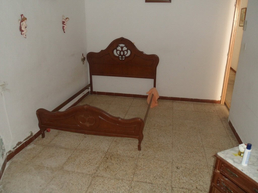 Bedroom with wooden bed frame in a town house in Freila, Granada.