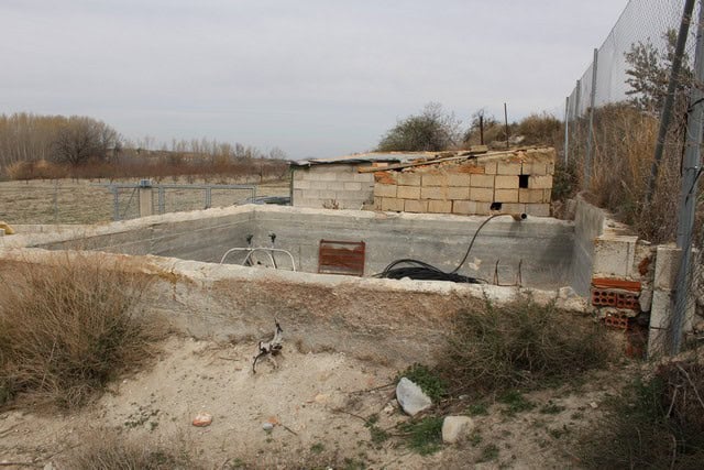 Abandoned rural property site in Caniles, Granada, showing unfinished construction and natural surro.