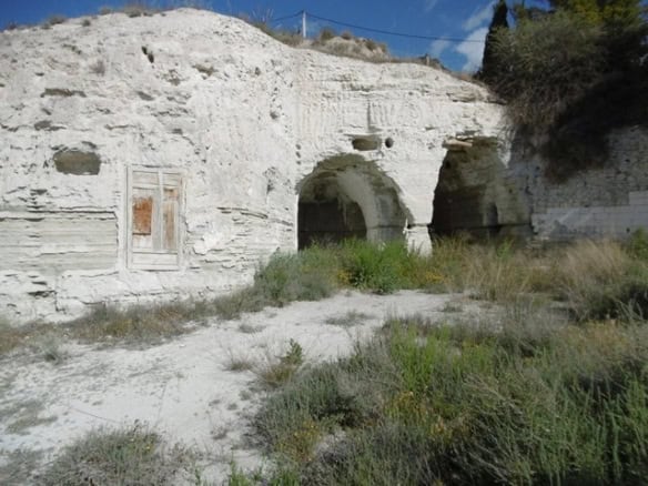 Cave house in Benamaurel, Granada, carved into white rock with arched entrances and surrounding natu.