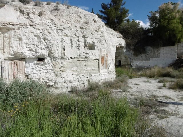 Cave house built into white rocky hillside in Benamaurel, Granada, with small windows and surrounded.